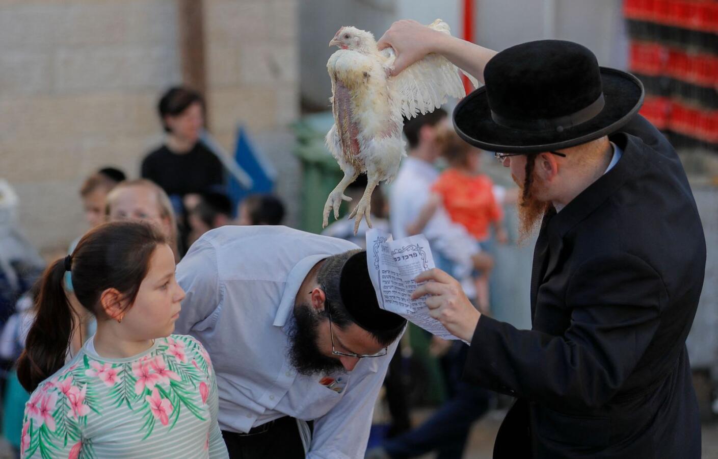 An ultra-Orthodox Jew swings a chicken over the head of a member of their family as they perform the Kapparot ceremony in an ultra-Orthodox neighbourhood in Jerusalem, on September 14, 2021. - Kapparot is a custom practised by some Jews, in which the sins of a person are symbolically transferred to a fowl, and is performed before Yom Kippur (Day of Atonement), the most important day in the Jewish calendar, which will start this year at sunset on September 15. (Photo by AHMAD GHARABLI / AFP) (Photo by AHMAD GHARABLI/AFP via Getty Images)