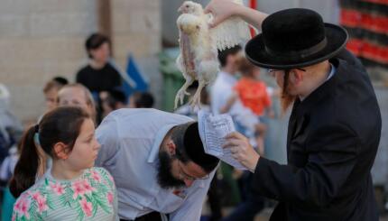 An ultra-Orthodox Jew swings a chicken over the head of a member of their family as they perform the Kapparot ceremony in an ultra-Orthodox neighbourhood in Jerusalem, on September 14, 2021. - Kapparot is a custom practised by some Jews, in which the sins of a person are symbolically transferred to a fowl, and is performed before Yom Kippur (Day of Atonement), the most important day in the Jewish calendar, which will start this year at sunset on September 15. (Photo by AHMAD GHARABLI / AFP) (Photo by AHMAD GHARABLI/AFP via Getty Images)