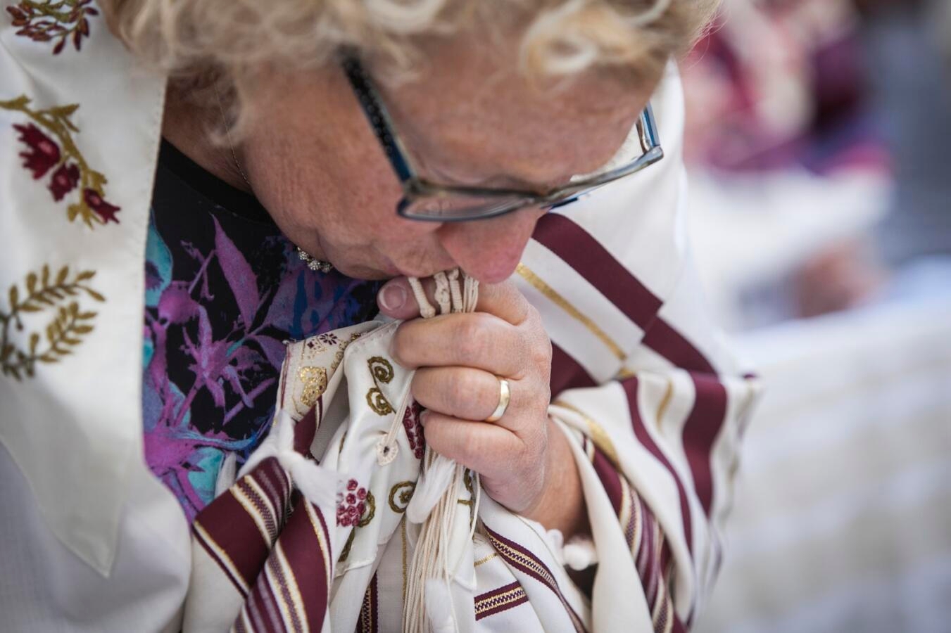 Photo of a woman wearing a tallit and kissing the fringes.