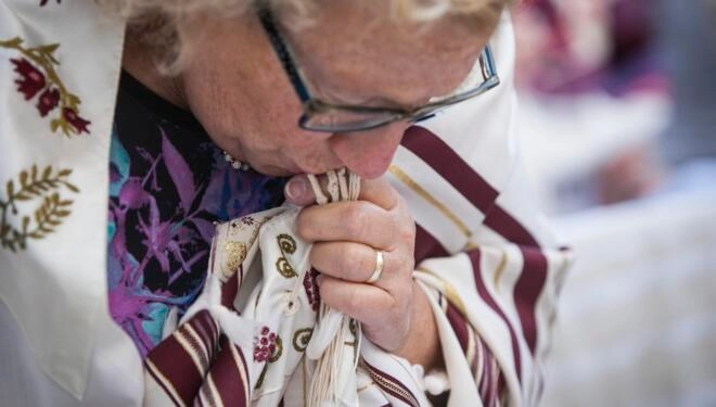 Photo of a woman wearing a tallit and kissing the fringes.