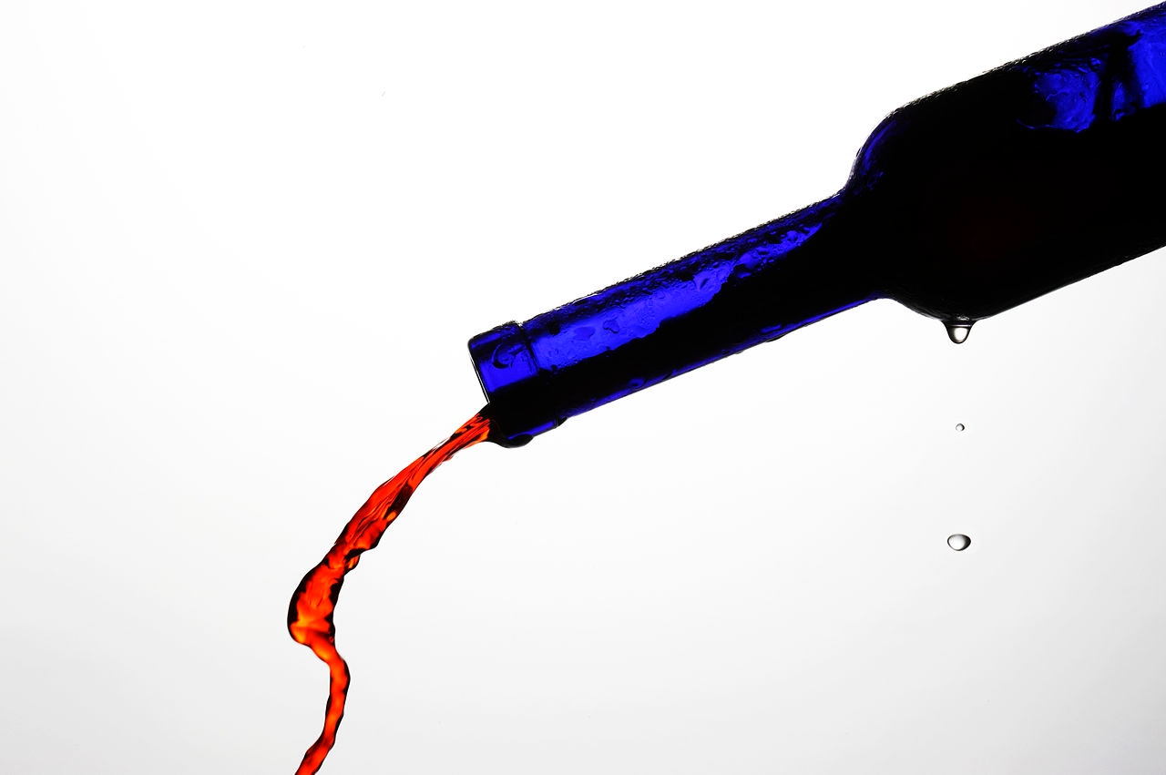 blue bottle pouring red wine against a whitebackground
