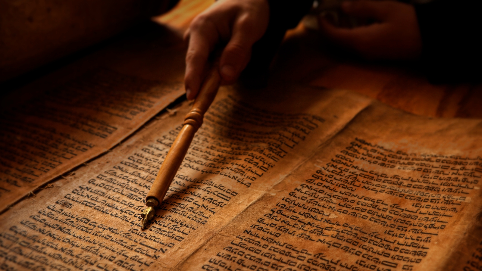 A picture of a pen pointing to a hebrew scroll.