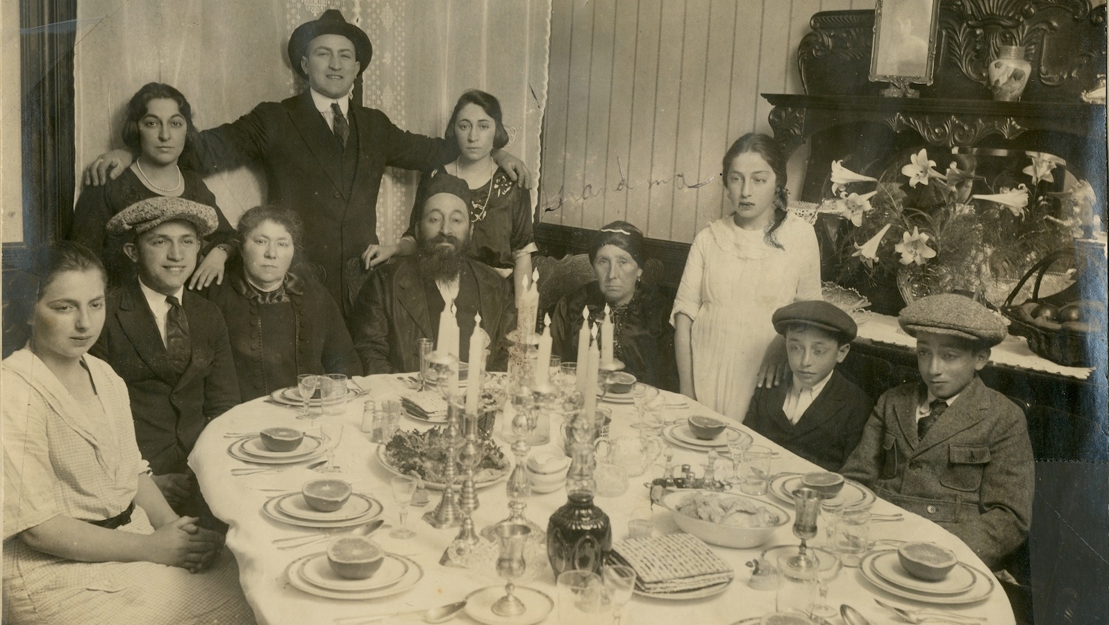 A black and white photo of a Passover seder in the 1920s. Grandparents, parents and children are pictured around a table decorated for a seder.