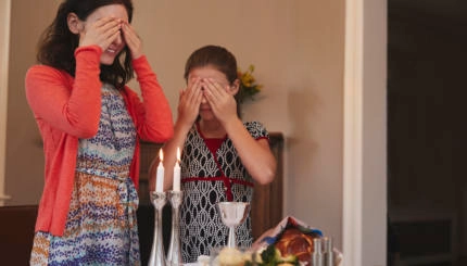 Jewish girl and mother cover eyes to recite Shabbat blessing