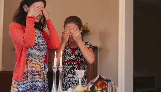 Jewish girl and mother cover eyes to recite Shabbat blessing