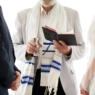 Image of a rabbi's hand holding a kiddush cup between two people getting married.