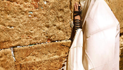 Photo of a man wrapped in a Jewish prayer shawl praying at the Western Wall.