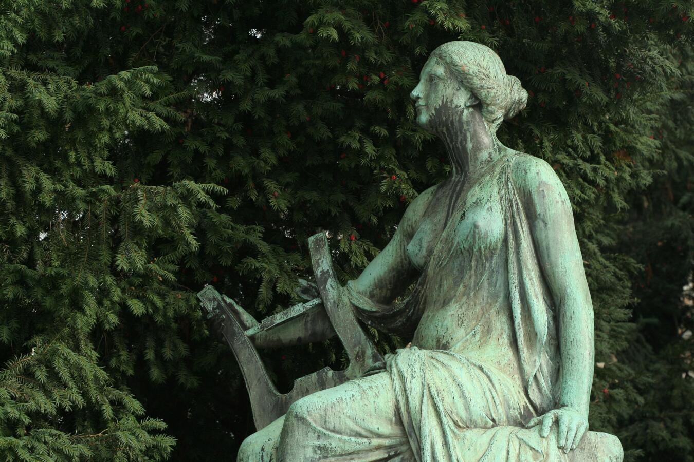 Weathered green statue of a woman playing a lyre.