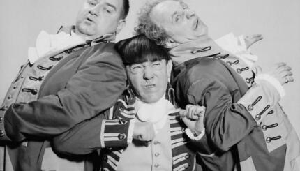 Three men in costume leaning on one another a grimacing.