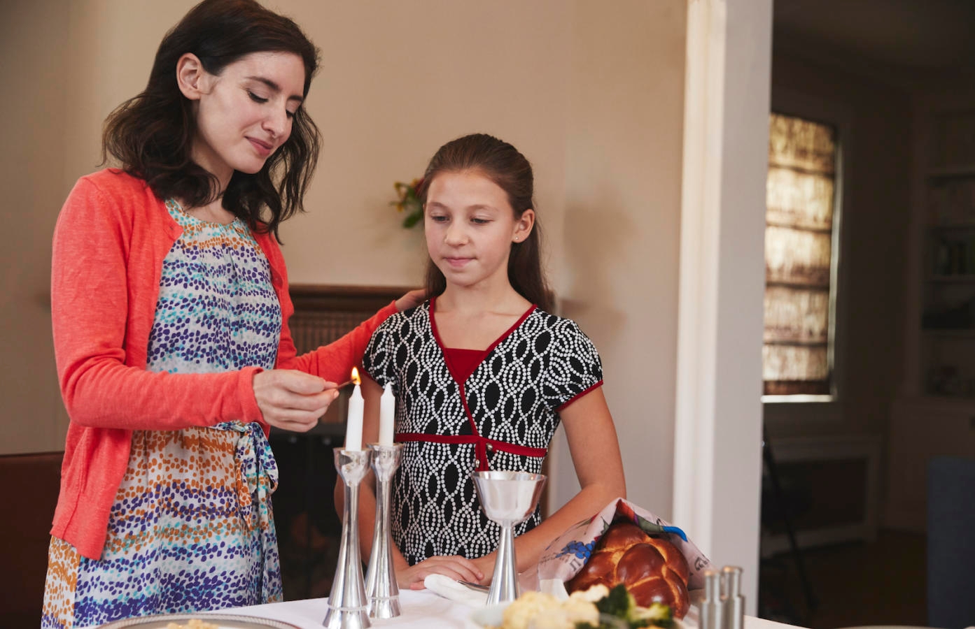 Jewish mother and daughter lighting candles for Shabbat meal