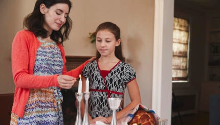 Jewish mother and daughter lighting candles for Shabbat meal