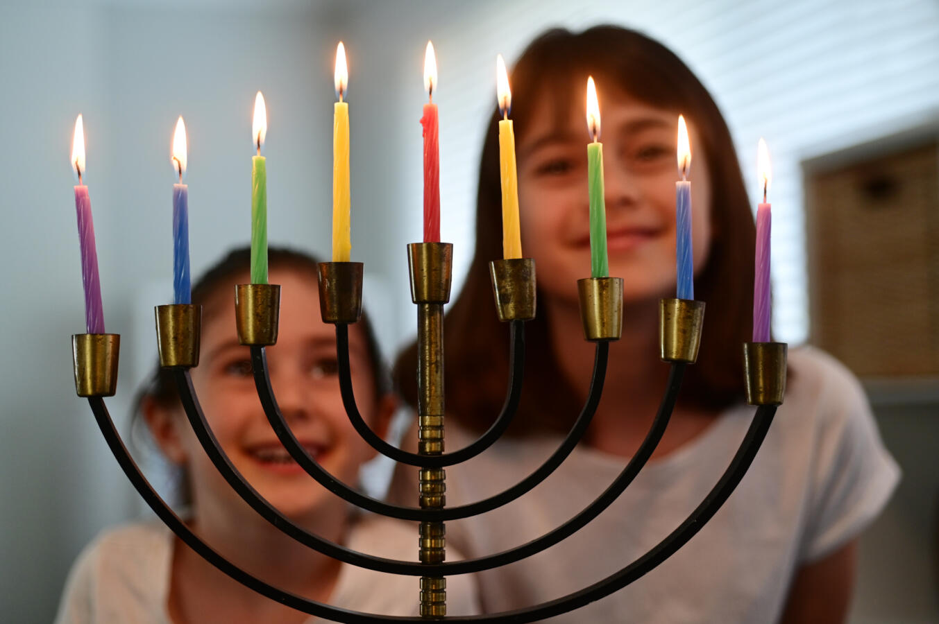 photo of sisters staring at a lit hanukkah menorah