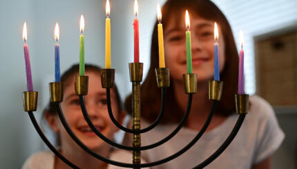 photo of sisters staring at a lit hanukkah menorah