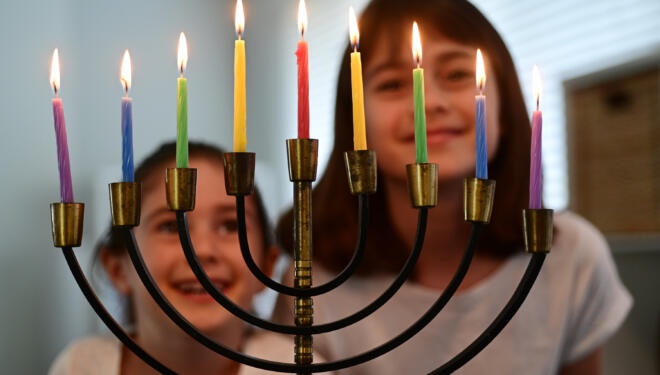 photo of sisters staring at a lit hanukkah menorah