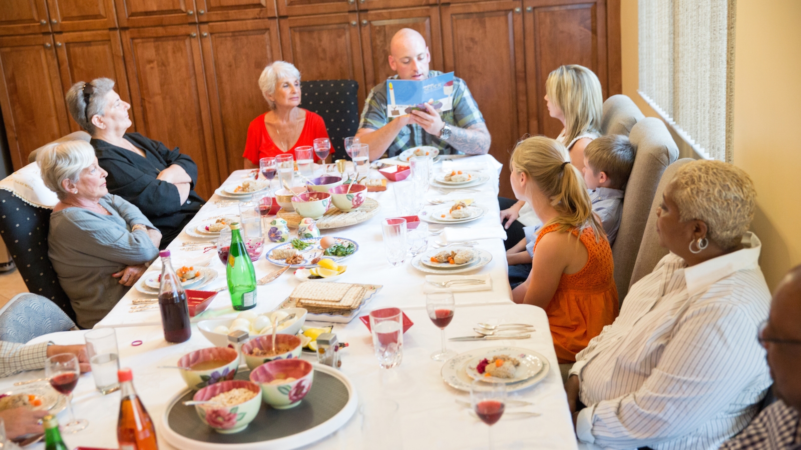 A family gathers for a Passover seder featuring many of the traditional Passover foods, like charoset, eggs and matzah. A man reads from a Haggadah.