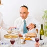 a Passover seder, including men wearing kippot or yarmulkes, and a table with matzo ball soup, wine, matzah and other traditional Passover foods