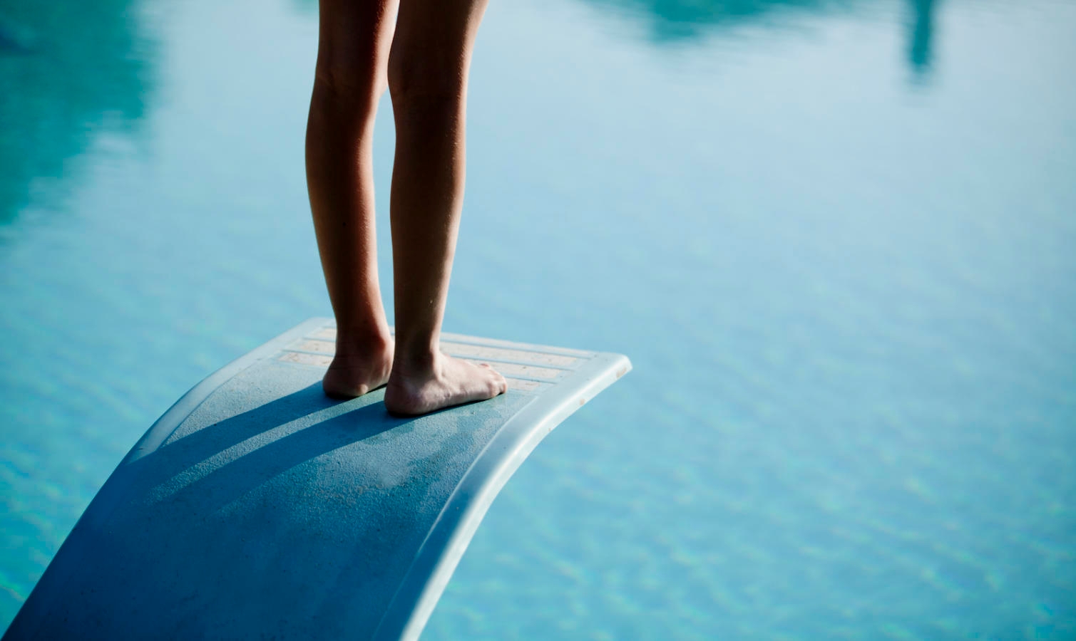 Shot of bare legs on diving board above blue water