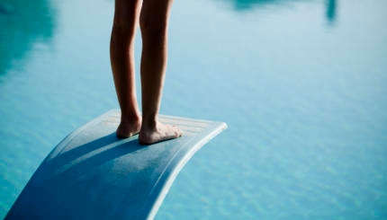 Shot of bare legs on diving board above blue water