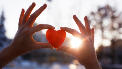 Woman hands holding red heart at sunset