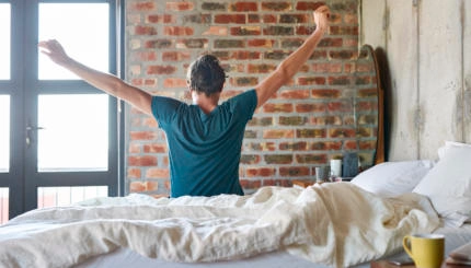 Rear view of young man stretching hands in bed