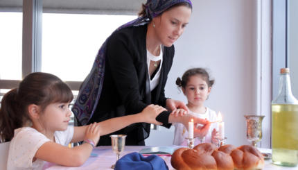 Jewish mother and daughters light Sabbath candle