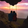 Couple on swing contemplating the sunset over the sea in a romantic view with heart shape.