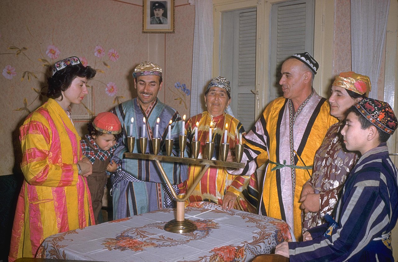 Jews in colorful costume cluster around a Hanukkah menorah.