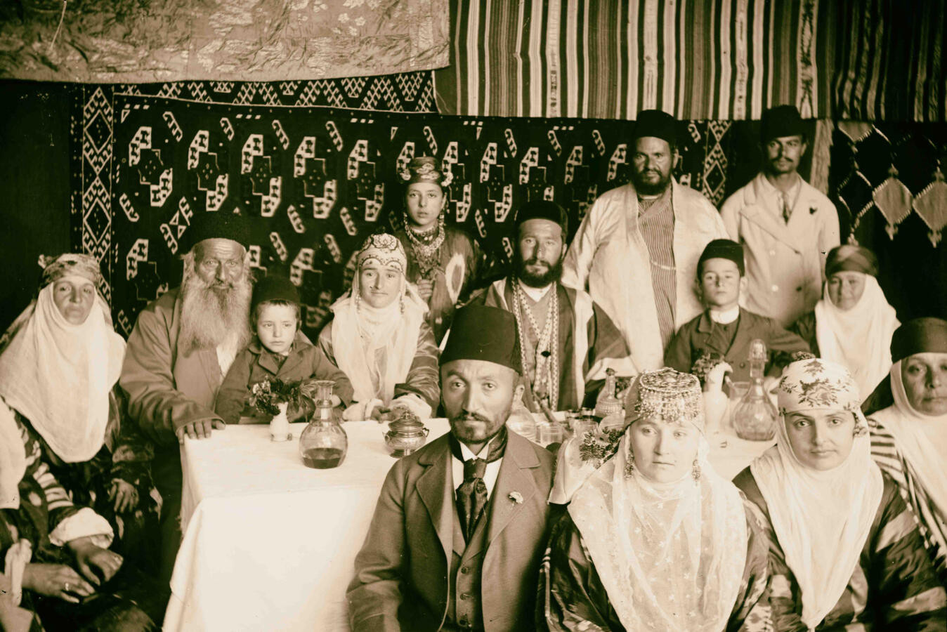 Sepia photograph of Bukharan Jews in a sukkah in traditional dress.