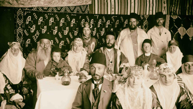 Sepia photograph of Bukharan Jews in a sukkah in traditional dress.
