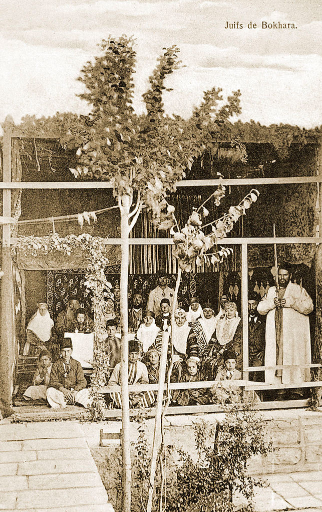 Black and white photo of Jews in a sukkah wearing traditional Bukharan costume.