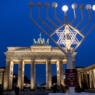 Two lights and the star shine on the Hanukkah chandelier in front of the illuminated Brandenburg Gate.