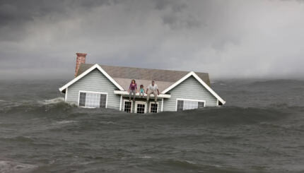 Family sitting on roof of house floating in sea