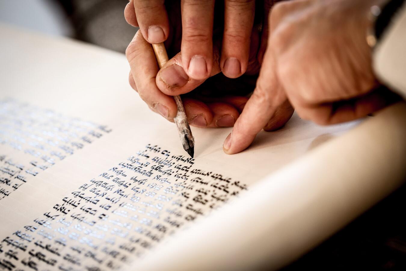 close up of hands scribing a torah scroll