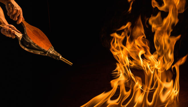 Man's hands stoking flames with bellows stoker