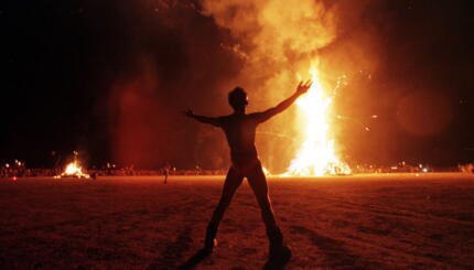 BLACK ROCK DESERT, UNITED STATES: A "Burning Man" participant holds up his arms as the wooden man effigy is burned at the conclusion of the week-long "Burning Man Festival" 06 September in the Black Rock Desert in the northwestern part of the state of Nevada. More than 15,000 people congregated at this man-made town in the desert to celebrate radical, creative self-expression. AFP PHOTO Mike NELSON/mn (Photo credit should read MIKE NELSON/AFP via Getty Images)
