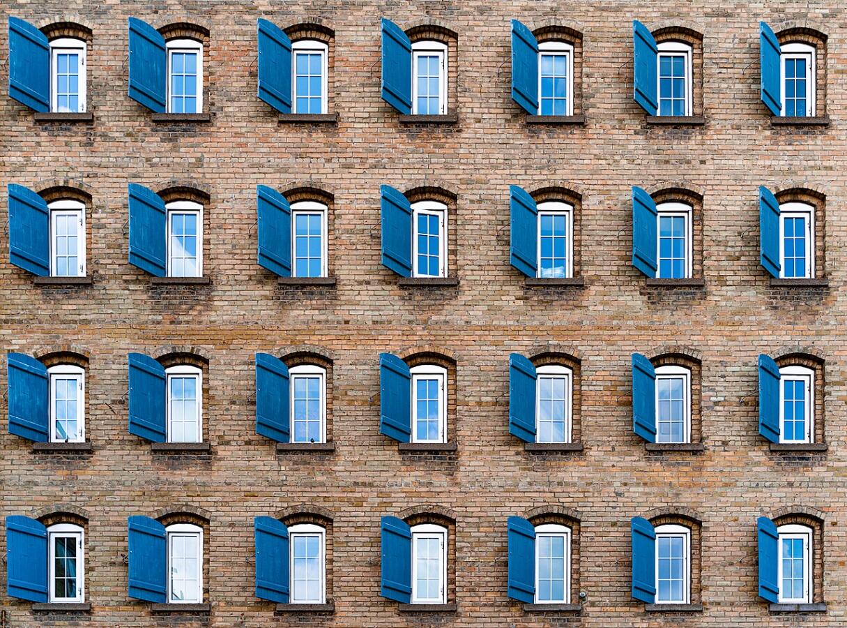Brick wall with rolws of windows, all with blue shutters.
