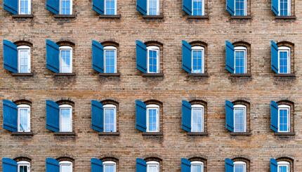 Brick wall with rolws of windows, all with blue shutters.