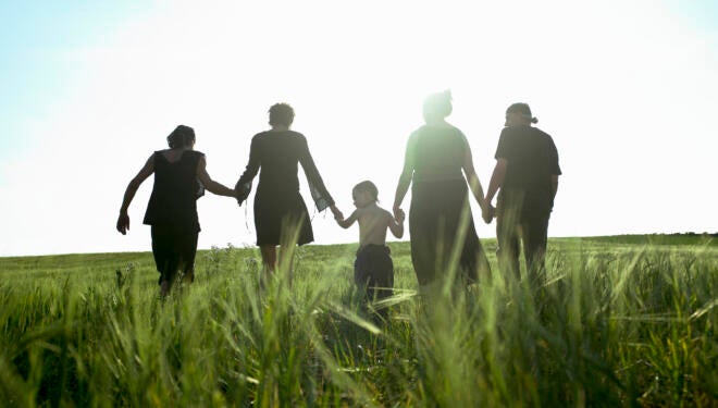 Sillhouette of people in a field holding hands.