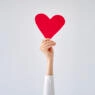 Female's hand holding red heart against white grey background.