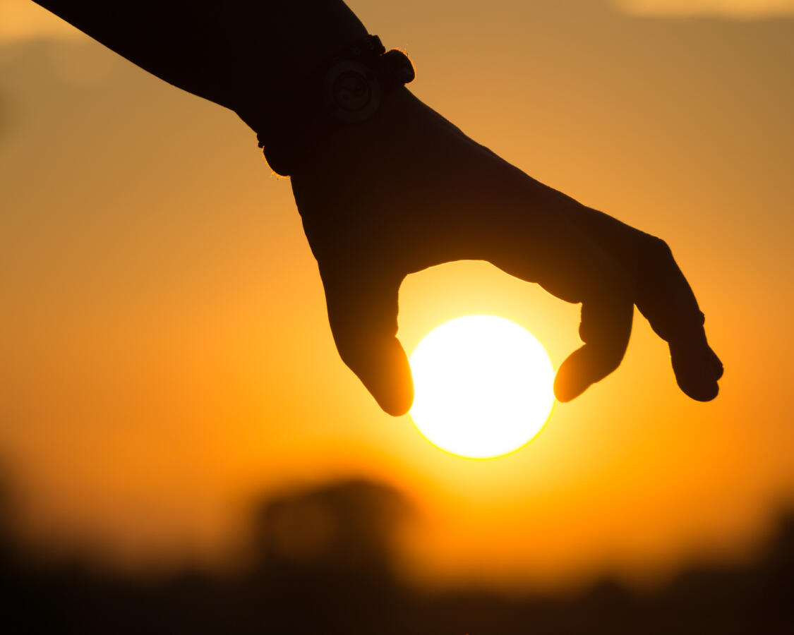 Cropped silhouette of hand holding sun against sky during sunset