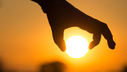 Cropped silhouette of hand holding sun against sky during sunset