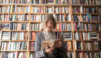 Senior woman reading book while standing against bookshelf at bookstore