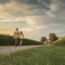 Caucasian father and daughter walking on dirt path by corn field