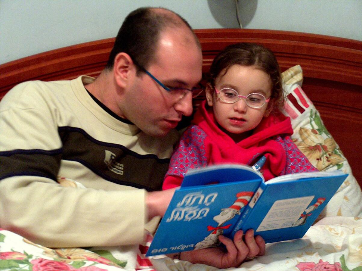 Photo of a father reading Cat in the Hat in Hebrew to his daughter.