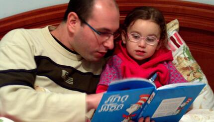 Photo of a father reading Cat in the Hat in Hebrew to his daughter.