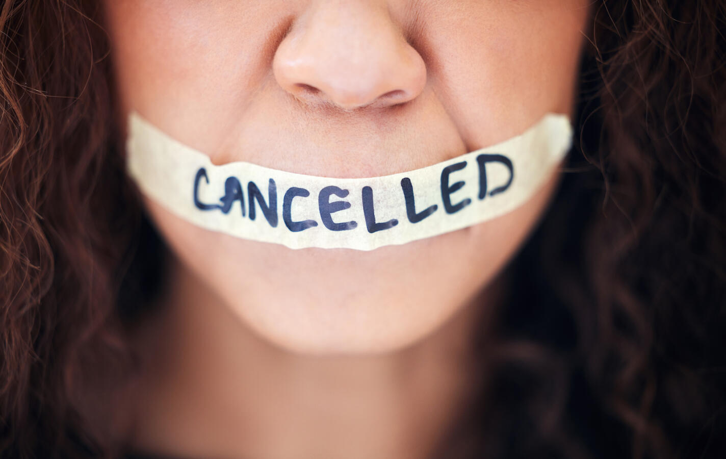 Closeup shot of an unrecognisable woman with tape on her mouth that has the word "cancelled" written on it