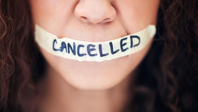 Closeup shot of an unrecognisable woman with tape on her mouth that has the word "cancelled" written on it