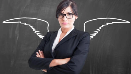 Photo of a woman standing at a blackboard with crossed arms and angel wings drawn behind her.