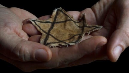A faded Jewish star badge resting in someone's hands.