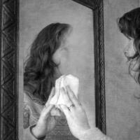 A woman uses a paper towel to wipe away her reflection in a mirror.